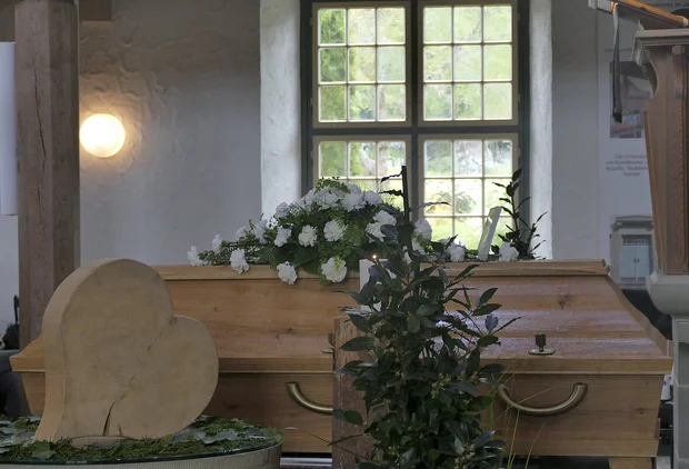 Aufgestellter Sarg mit Blumenbouquet in einer Kirche 
